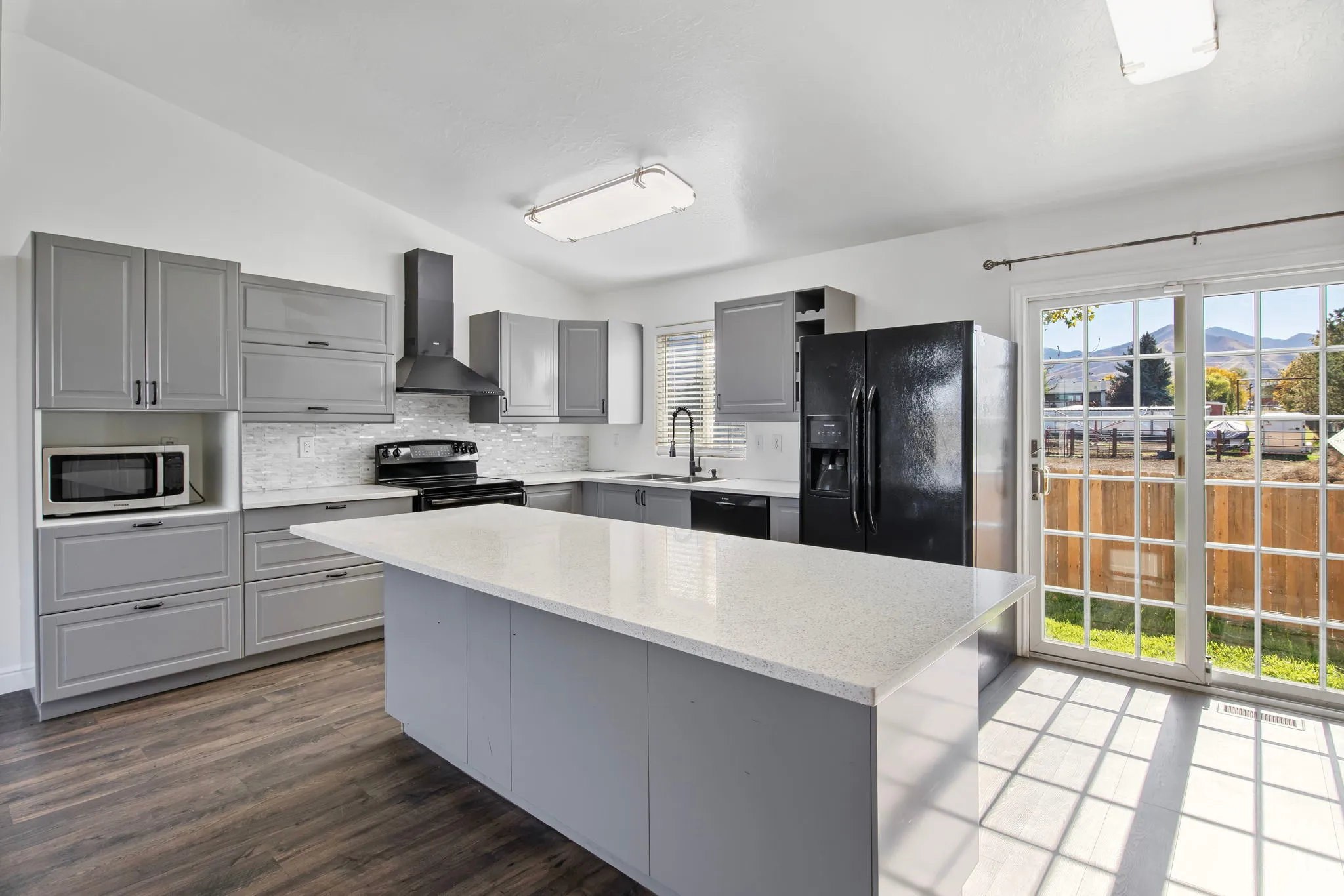 Kitchen with gray cabinets, lofted ceiling, wall chimney range hood, black appliances, and decorative backsplash