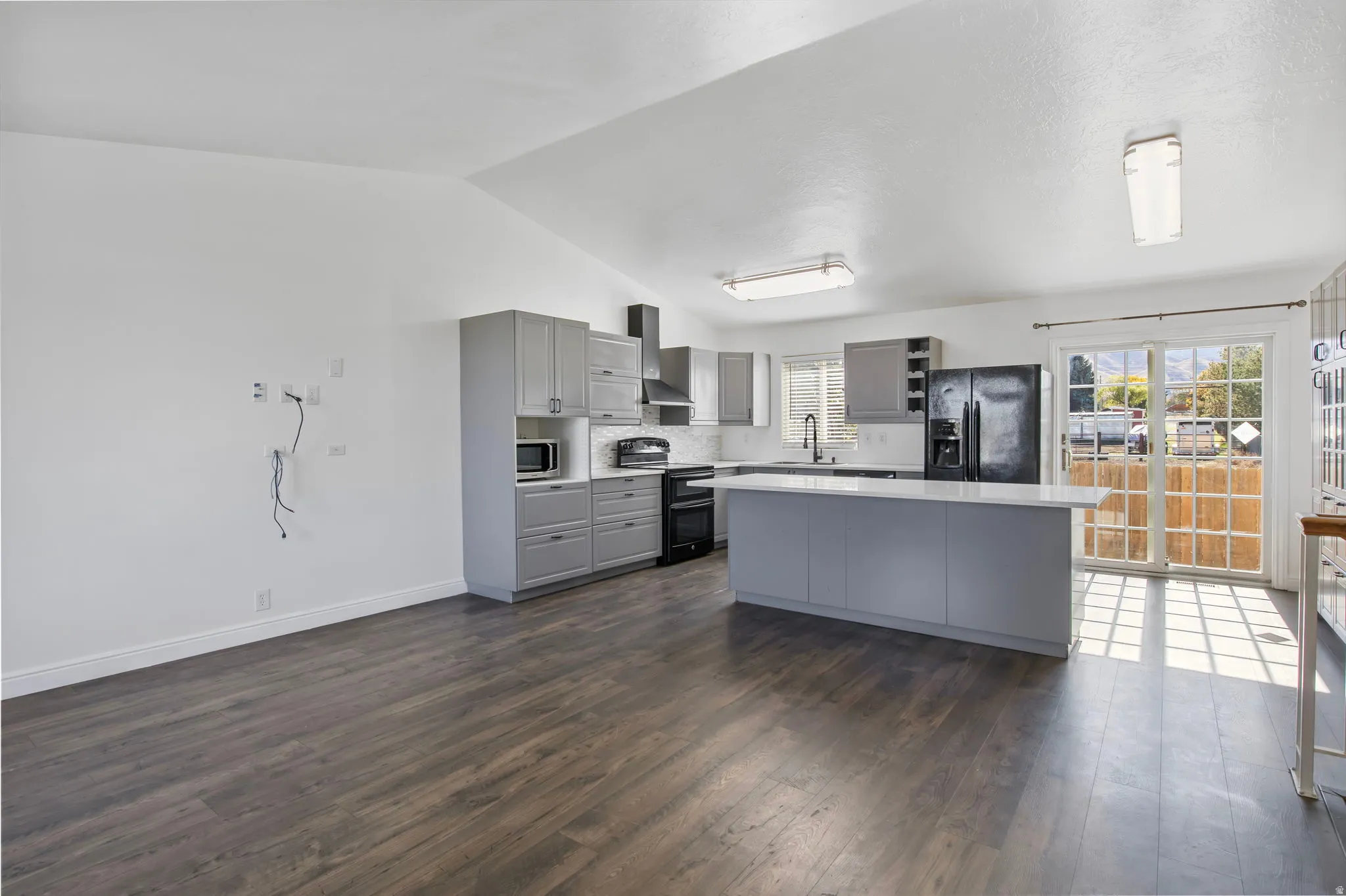 Kitchen featuring gray cabinets, black appliances, light countertops, vaulted ceiling, and dark wood-style floors