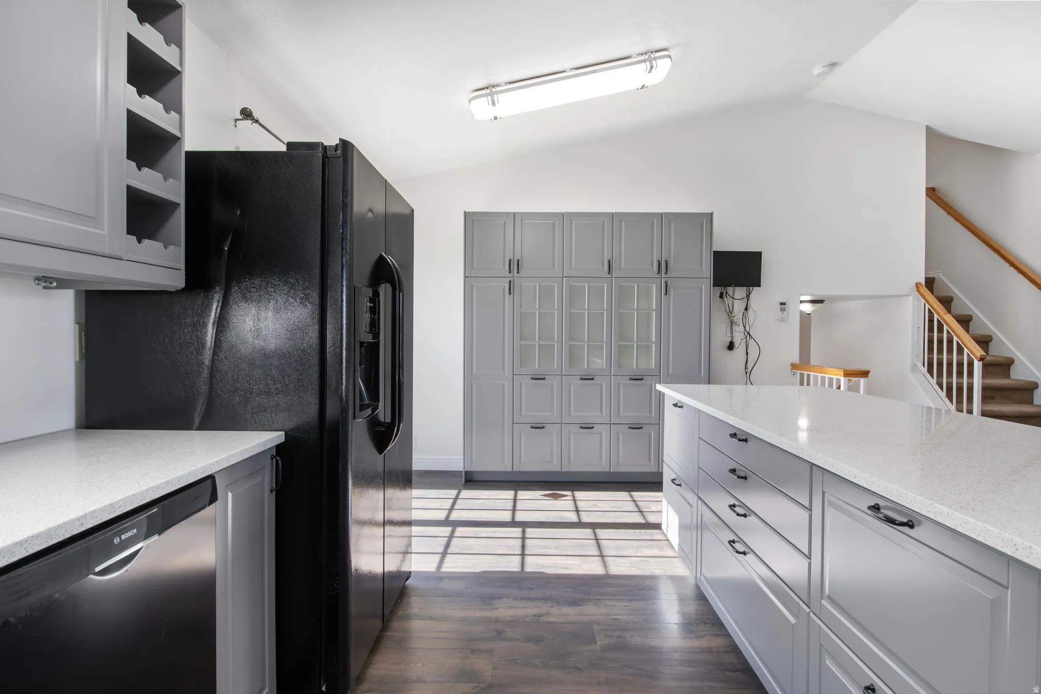 Kitchen featuring gray cabinetry, dishwasher, light stone counters, lofted ceiling, and dark wood finished floors