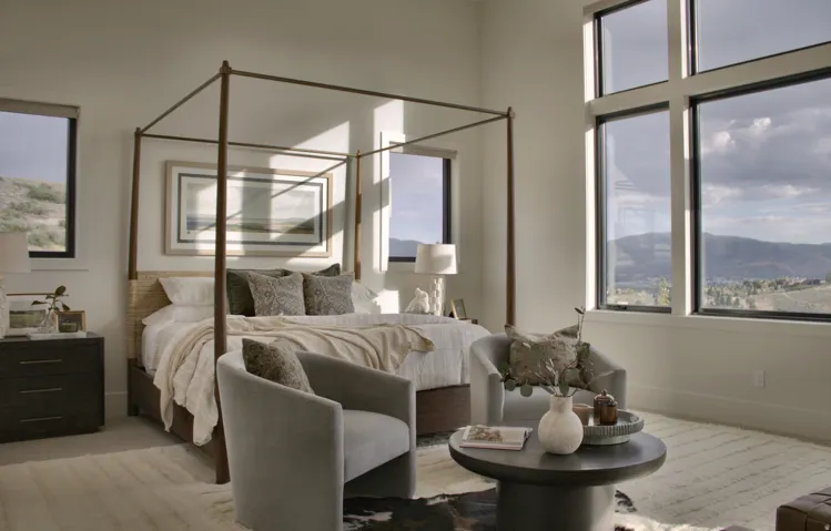 Expansive windows with mountain scenery, a large bed with a woven headboard, and a built-in nightstand with a table lamp