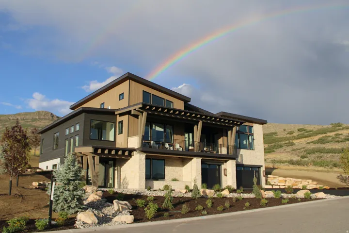 Multi-level contemporary exterior with stone accents, wood-finish siding, multiple windows, and an upper-level balcony with a pergola