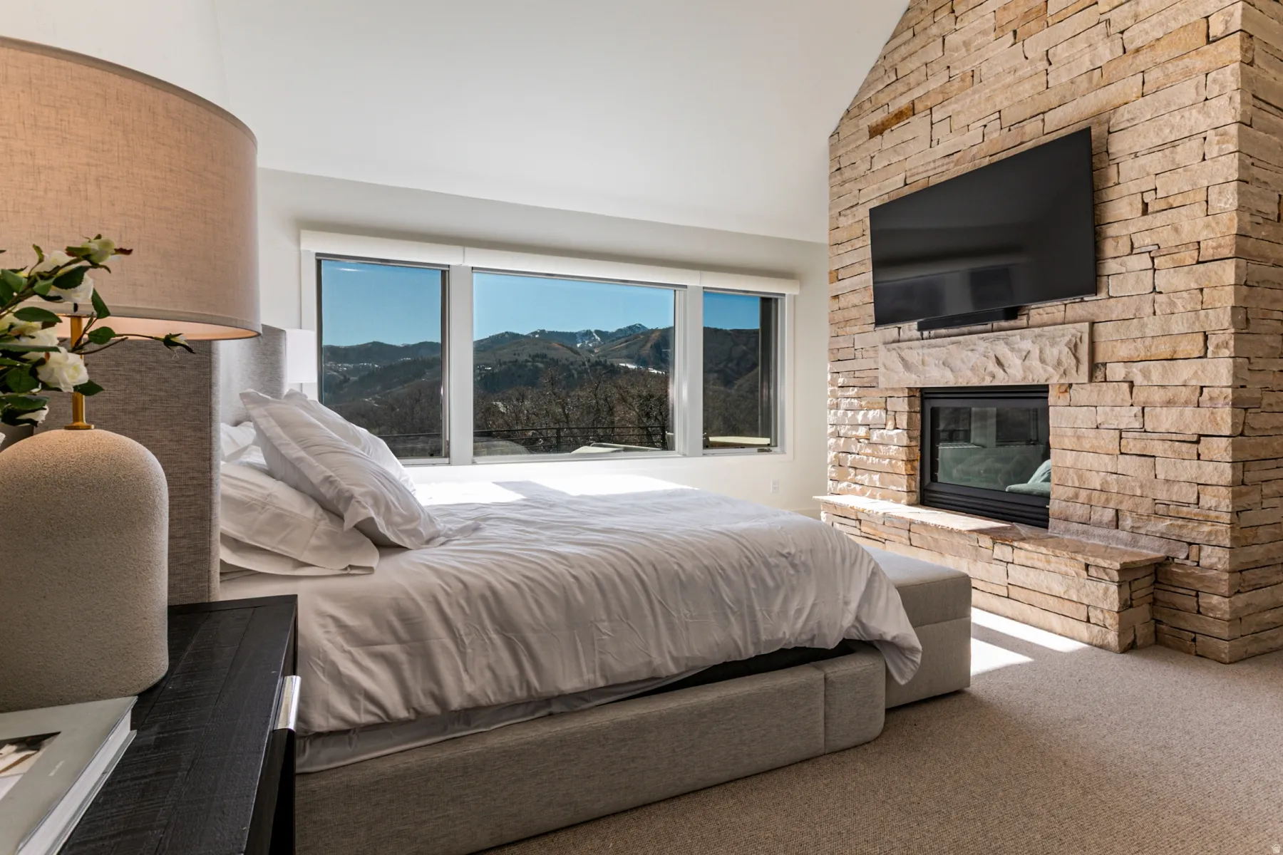Bedroom with lofted ceiling, carpet flooring, and a stone fireplace