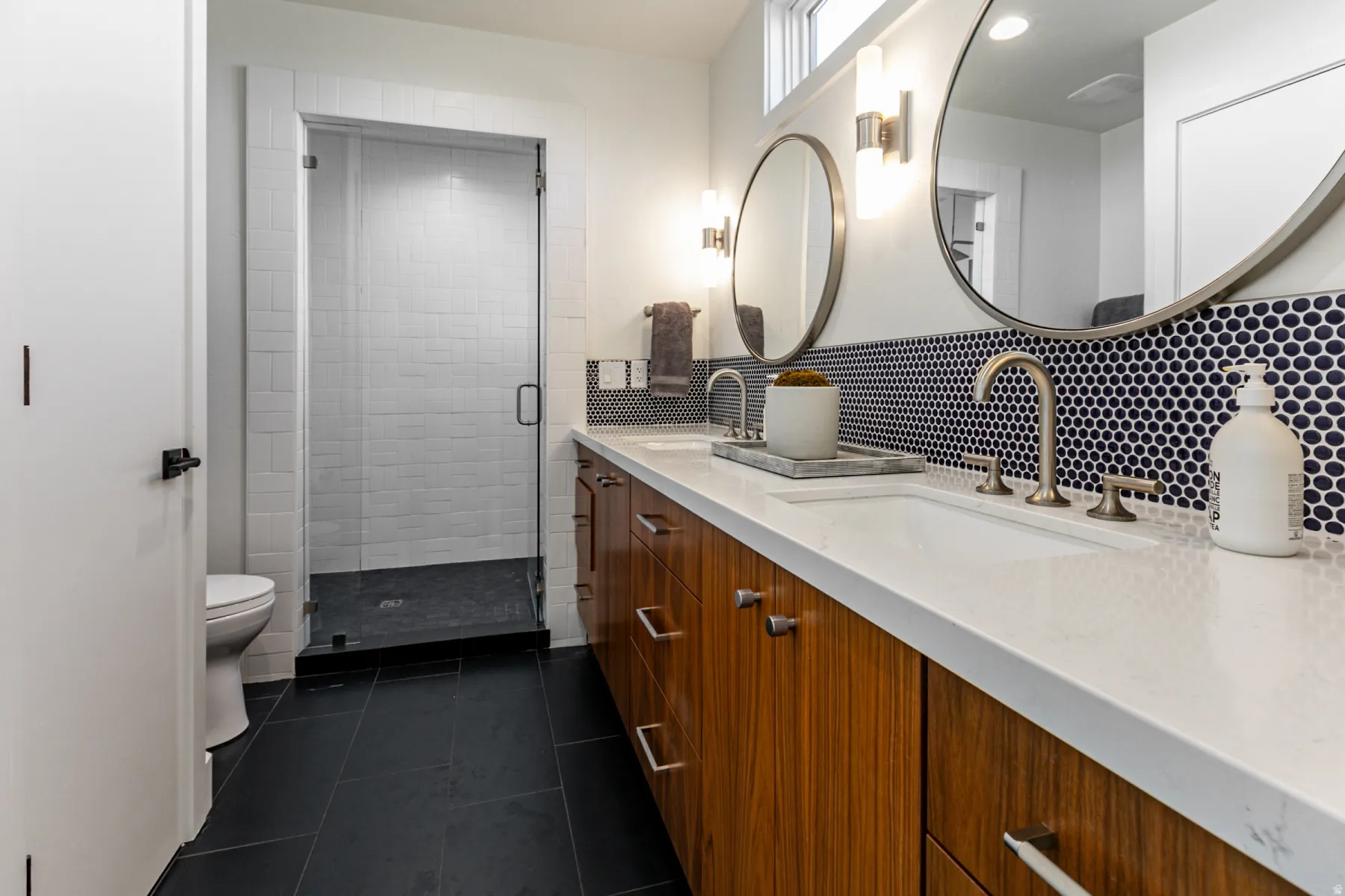 Full bath with double vanity, dark tile patterned flooring, a shower stall, and decorative backsplash
