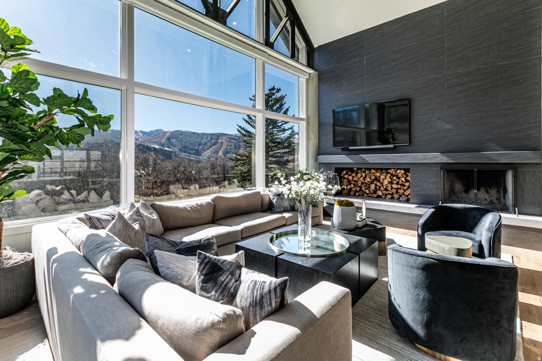 Living room featuring a fireplace with raised hearth, wood finished floors, a towering ceiling, and plenty of natural light