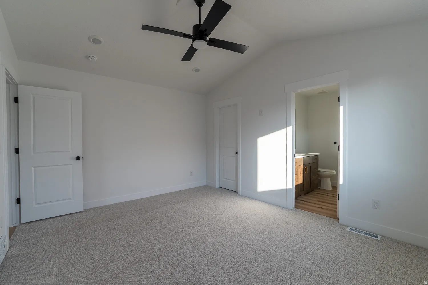 Unfurnished bedroom with vaulted ceiling, light carpet, ensuite bath, and ceiling fan