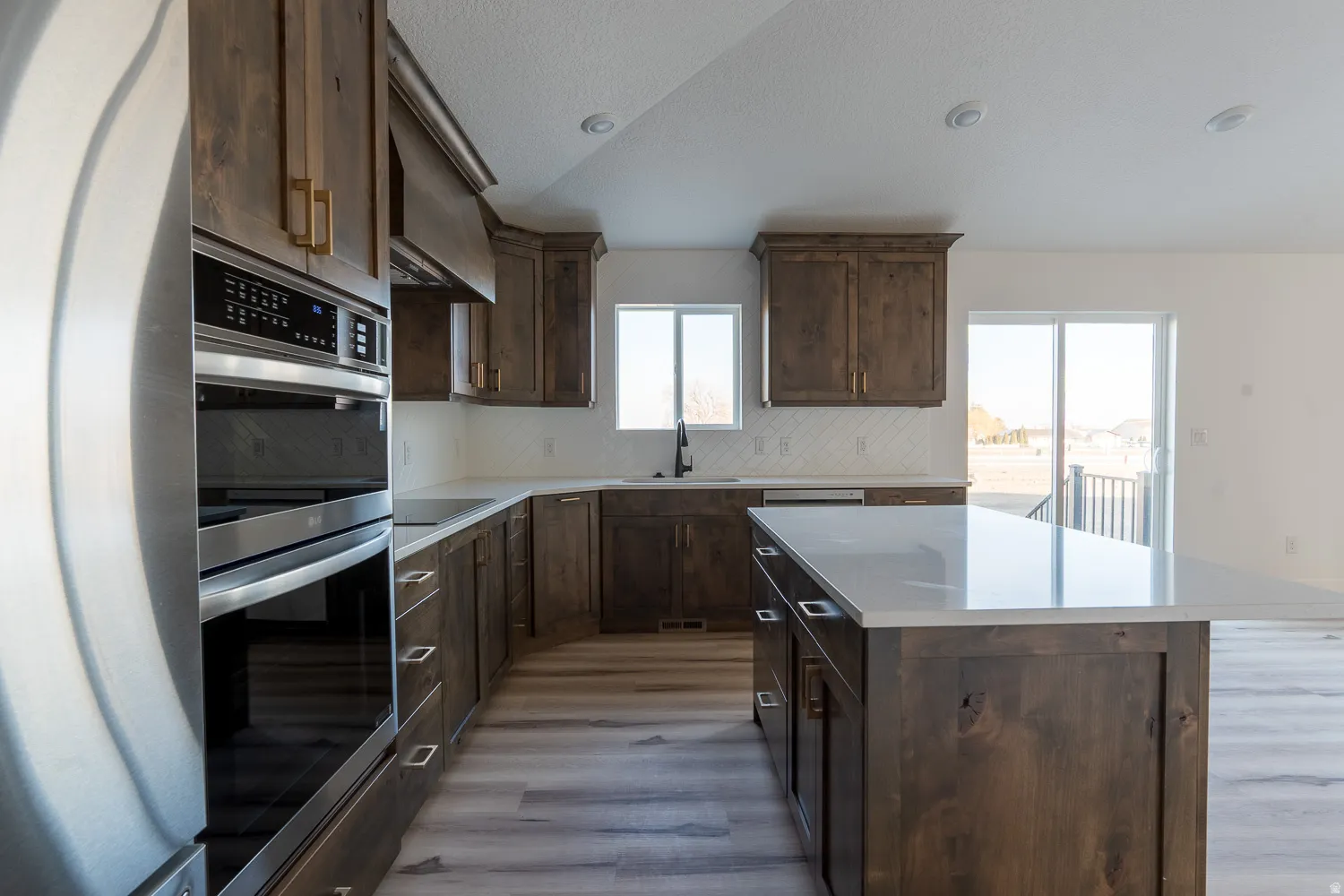 Kitchen with double oven, dark brown cabinetry, a center island, and backsplash