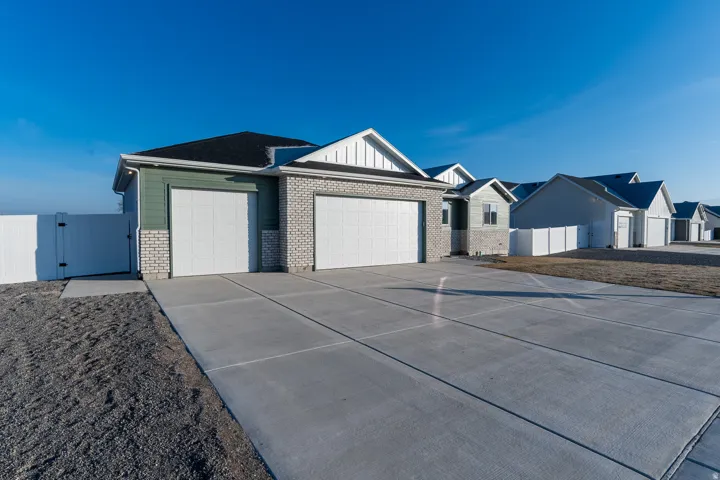 Single story home featuring a gate, an attached garage, concrete driveway, brick siding, and board and batten siding