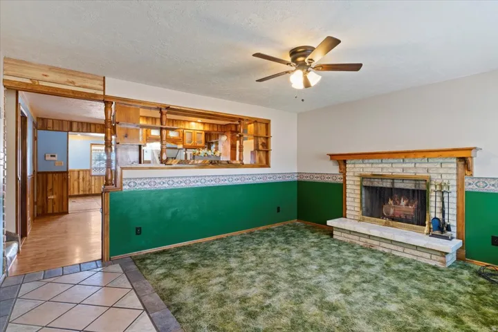 Unfurnished living room with tile patterned floors, a wainscoted wall, a textured ceiling, a fireplace, and ceiling fan