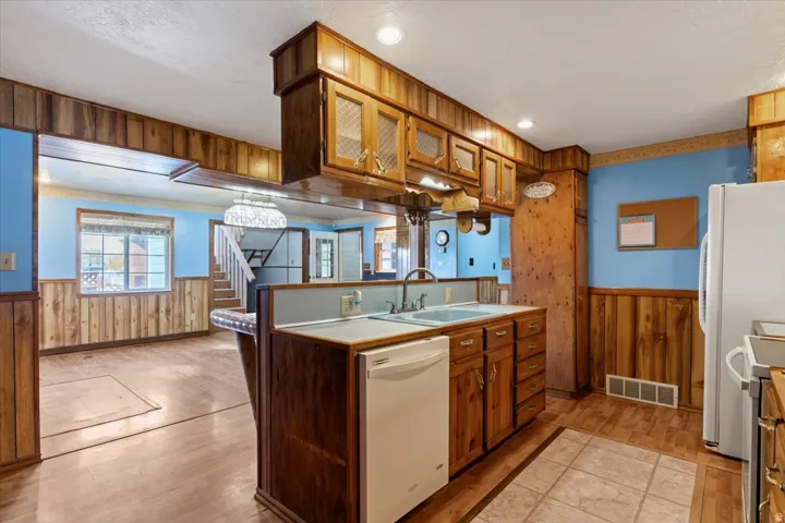 Kitchen with wooden walls, wainscoting, light wood-style floors, white appliances, and brown cabinetry