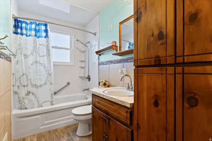 Bathroom with shower / bath combo, vanity, tile walls, and dark wood-type flooring