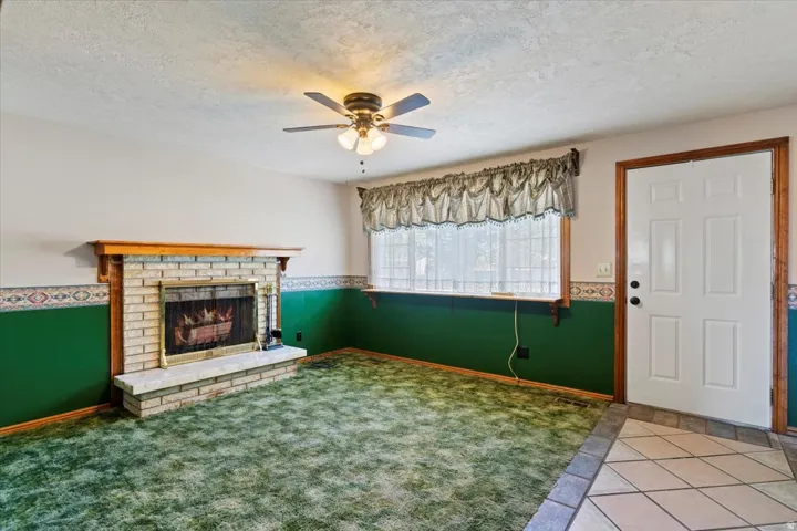 Unfurnished living room with a textured ceiling, a fireplace, tile patterned flooring, ceiling fan, and carpet