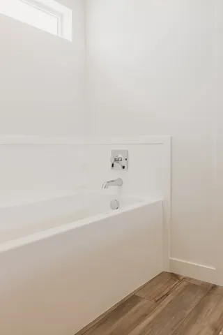 Built-in bathtub with chrome fixtures, wood-finish flooring, and white walls