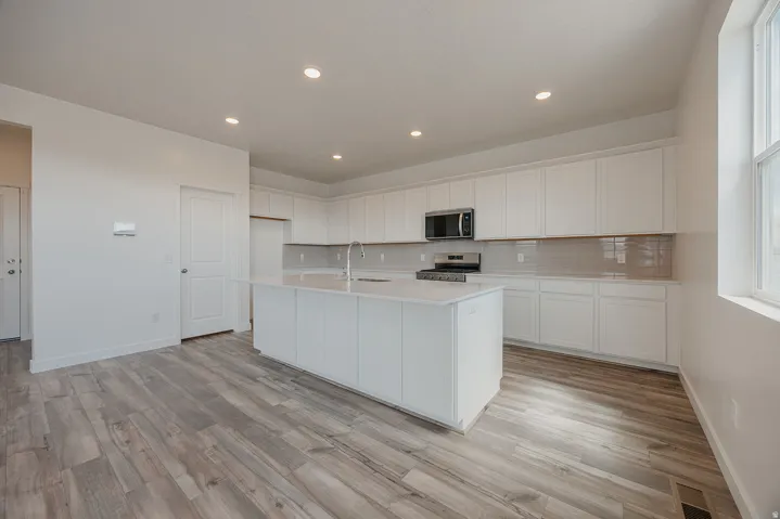 Open-concept kitchen with a central island, recessed lighting, white cabinetry, integrated stainless steel appliances, and wood-finish flooring