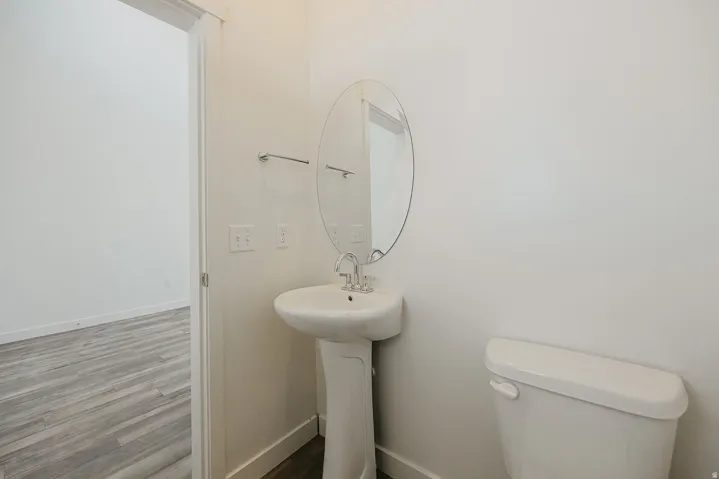 Pedestal sink with chrome faucet, oval mirror, and white toilet