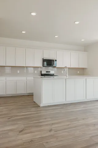 White cabinetry, stainless steel appliances, recessed lighting, wood-finish flooring, and a central island