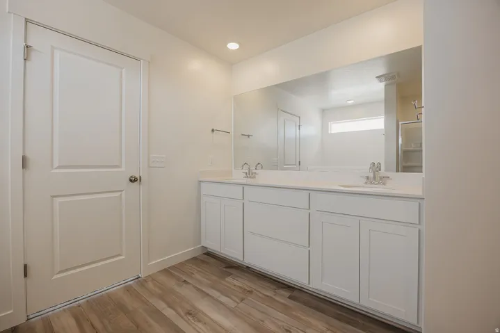 Dual vanity with undermount sinks, wood-finish flooring, and a full-width mirror