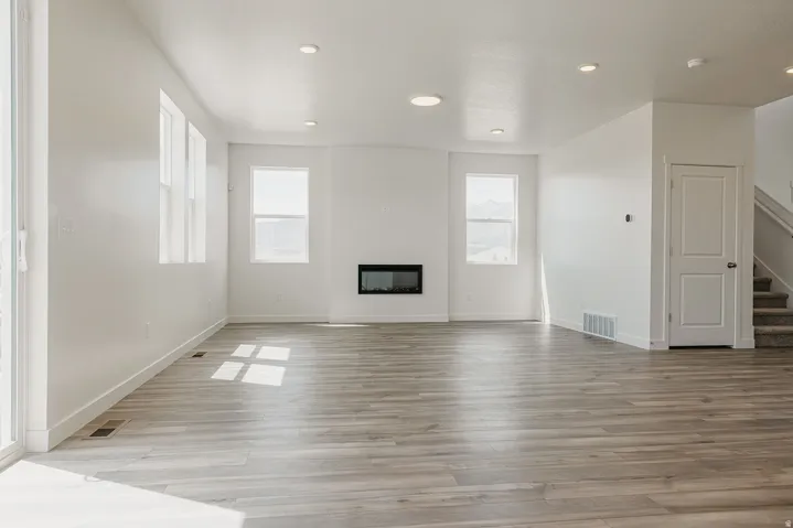 Spacious room featuring wood-finish flooring, multiple windows, a built-in electric fireplace, recessed lighting, and a sliding glass door