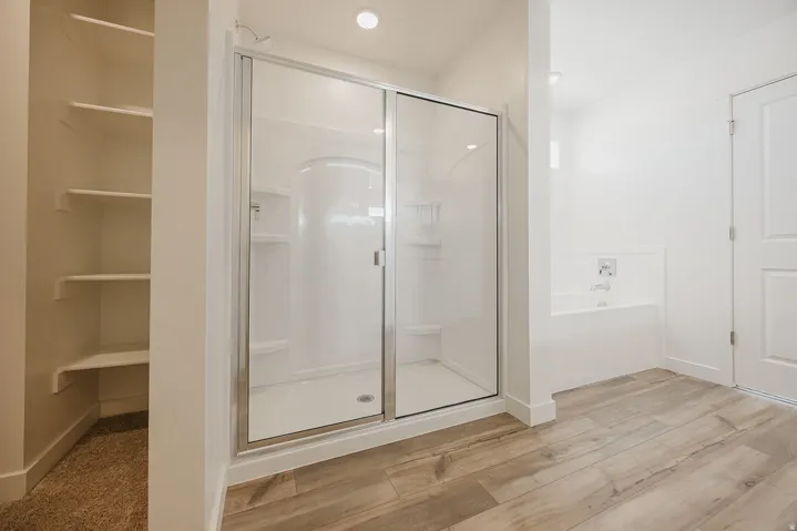 Walk-in shower with clear glass enclosure, built-in bathtub, and wood-finish flooring
