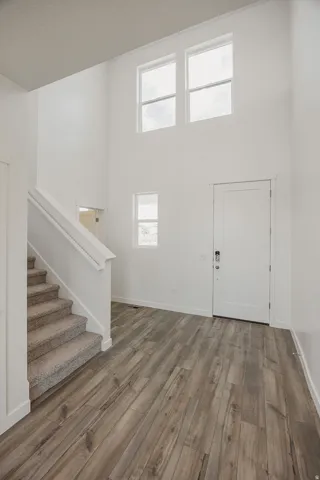 Two-story foyer with high ceilings, wood-finish flooring, white walls, and a staircase with carpeted treads