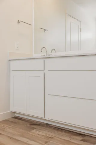 White vanity with integrated sink, chrome faucet, and wood-finish flooring