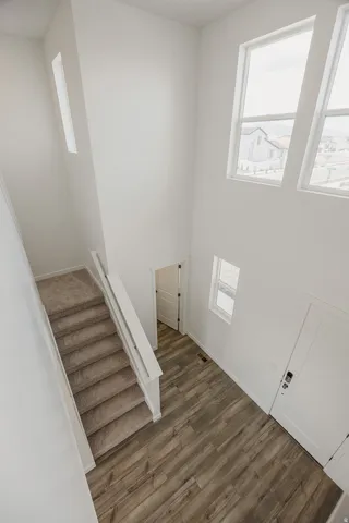 Two-story entry with wood-finish flooring, a carpeted staircase with white railings, and tall windows providing natural light