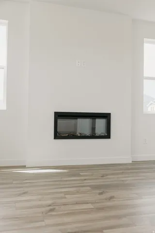 Integrated linear fireplace with a black frame, light wood-finish flooring, and white walls