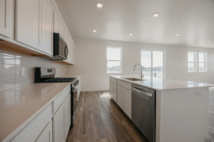 Modern kitchen featuring white cabinetry, light-colored countertops, stainless steel appliances, a large island with an integrated sink, and wood-finish flooring
