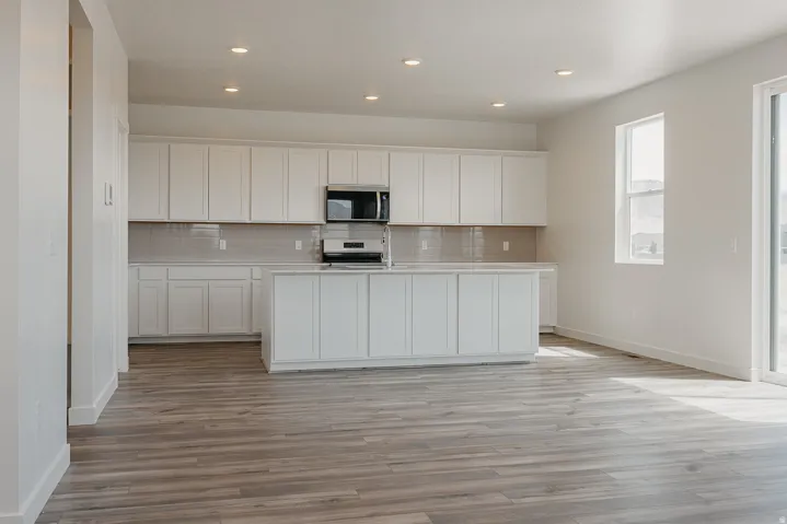 Kitchen featuring white cabinetry, light gray tile backsplash, stainless steel microwave, and a central island