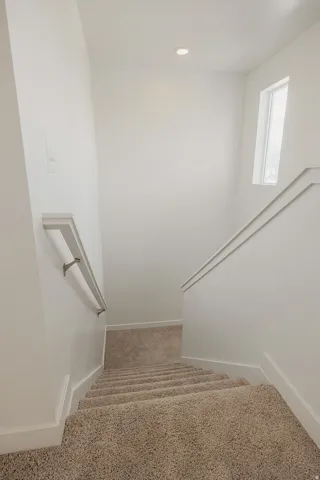 Staircase featuring neutral carpeting, a recessed ceiling light, a window, and white wall paneling