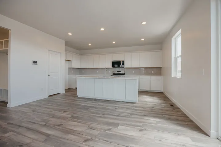 Open-concept kitchen featuring white cabinetry, a center island, stainless steel appliances, and wood-finish flooring