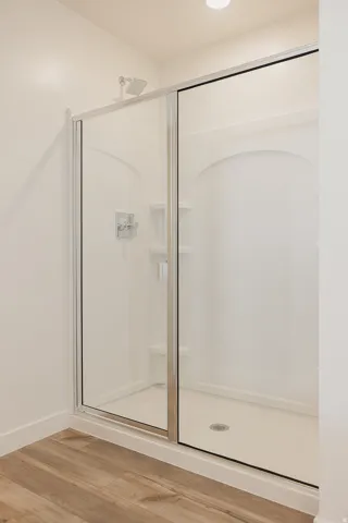 Shower enclosure with sliding glass doors, chrome fixtures, built-in shelving, and wood-finish flooring