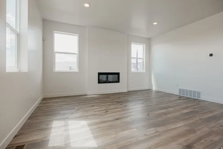 Spacious interior featuring wood-finish flooring, an integrated electric fireplace, multiple windows, recessed lighting, and crisp white walls