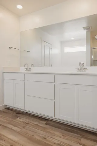 Dual vanity with integrated sinks, white cabinetry, wood-finish flooring, and a large wall-mounted mirror