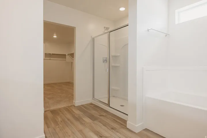 Wood-finish flooring, glass-enclosed shower, built-in bathtub, and recessed lighting
