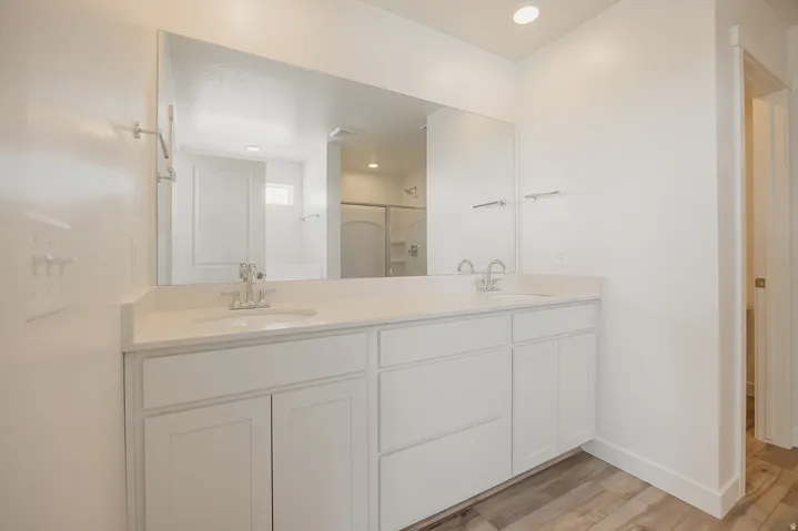 Dual vanity with white cabinetry and integrated sinks, a large wall-mounted mirror, and wood-finish flooring