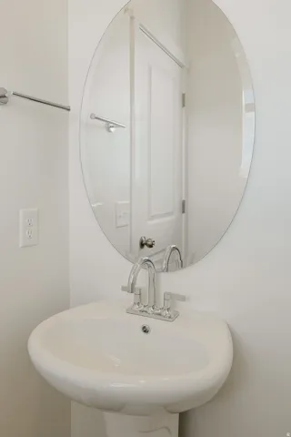 Pedestal sink with chrome faucet, oval mirror, and chrome towel bar