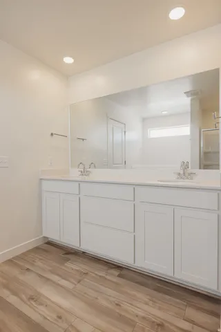 Double vanity with white cabinetry, wood-finish flooring, recessed lighting, and a large wall-mounted mirror