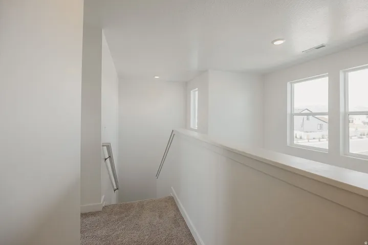 Upper-level landing with neutral carpeting, recessed ceiling lighting, and multiple windows