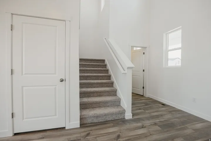 High ceilings, light wood-finish flooring, white walls, and a carpeted staircase with white railings