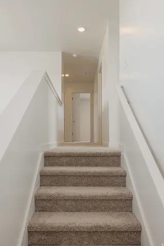Carpeted staircase with white risers and handrails, leading to a hallway with recessed lighting