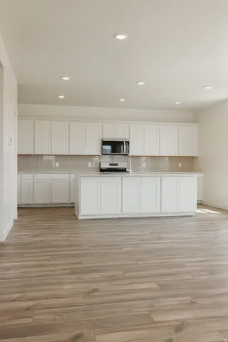 Kitchen featuring white shaker-style cabinetry, a large central island, stainless steel appliances, a subway tile backsplash, and recessed lighting