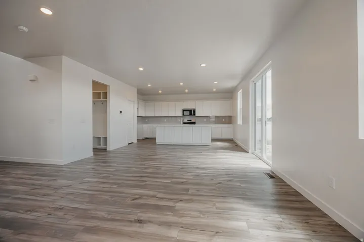 Spacious open-concept living area featuring wood-finish flooring, recessed lighting, and a contemporary kitchen with white cabinetry