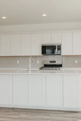 Bright kitchen featuring recessed lighting, white shaker-style cabinetry, a stainless steel microwave and gas range, and a light-toned backsplash
