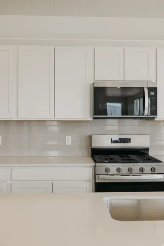 White shaker-style cabinetry, stainless steel microwave, gas range, light-toned countertops, and subway tile backsplash