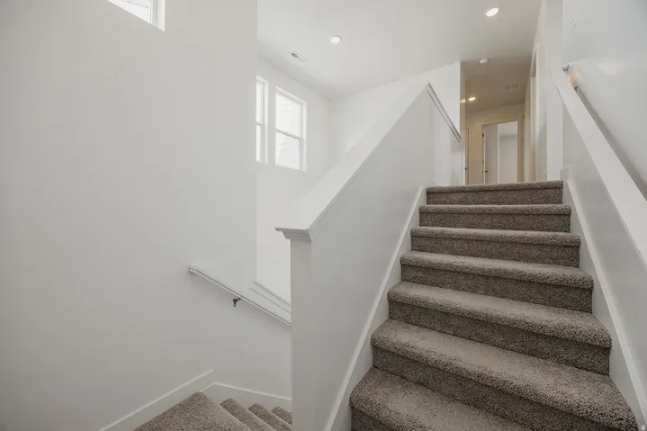 Carpeted stairway with white painted risers and handrails, featuring recessed lighting and natural light from upper-level windows