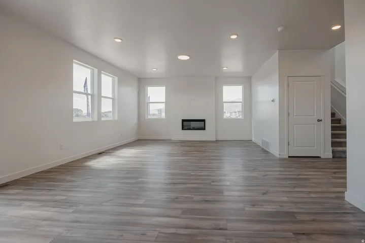 Spacious room featuring wood-finish flooring, recessed lighting, multiple windows, a built-in fireplace, and a staircase with carpeted treads