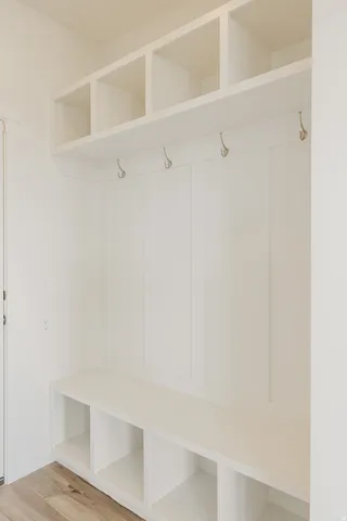 Built-in mudroom bench with storage cubbies, upper shelving, wall paneling, and wall-mounted hooks