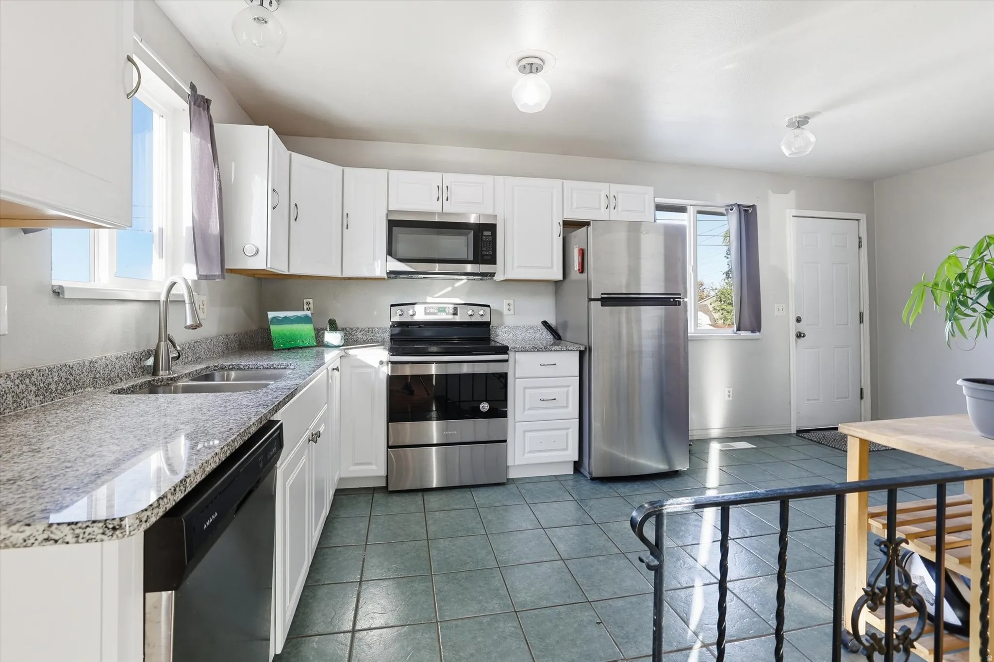 Kitchen featuring appliances with stainless steel finishes, white cabinetry, dark tile patterned floors, and light stone counters