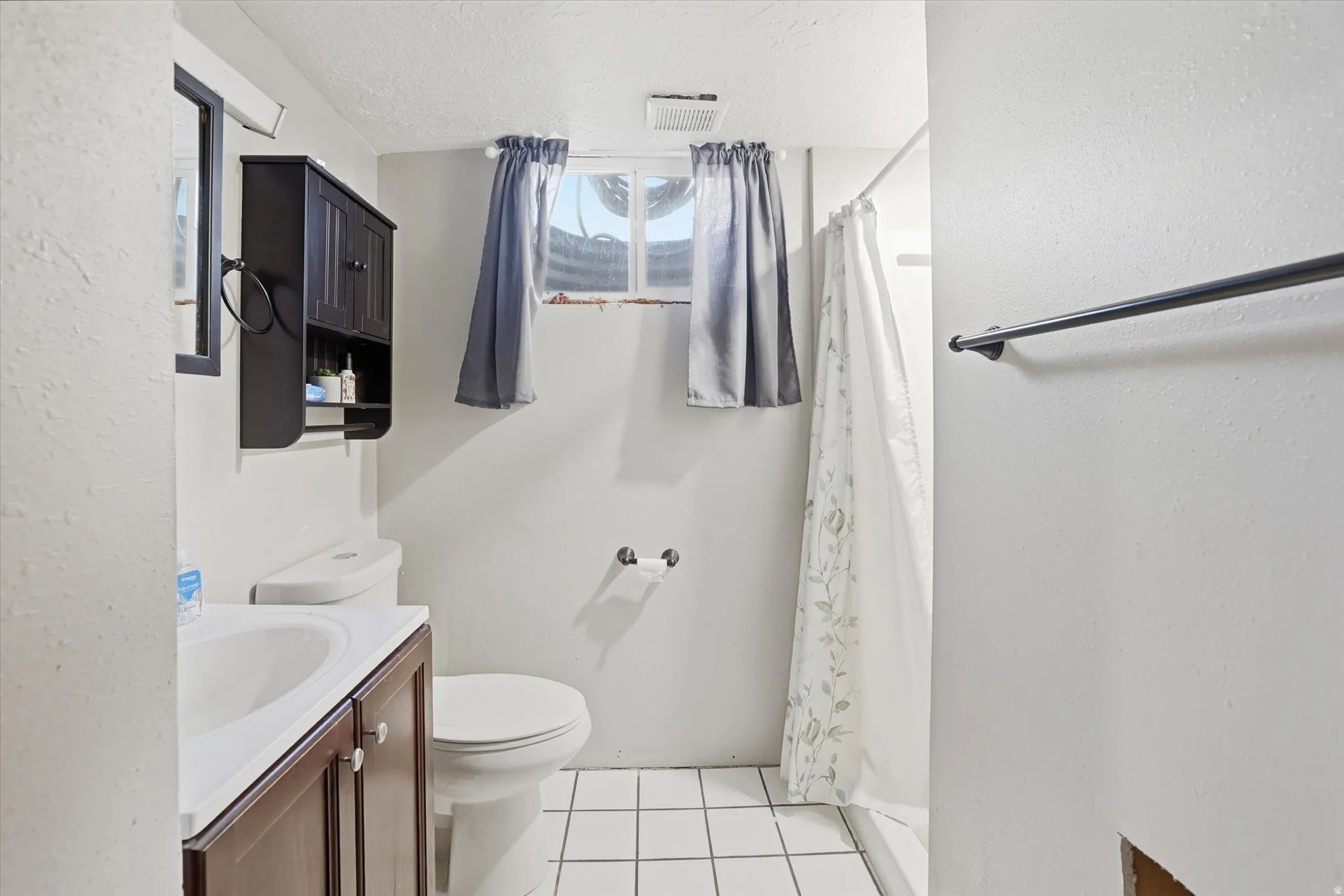 Bathroom with light tile patterned flooring, a shower with shower curtain, a textured ceiling, vanity, and a textured wall