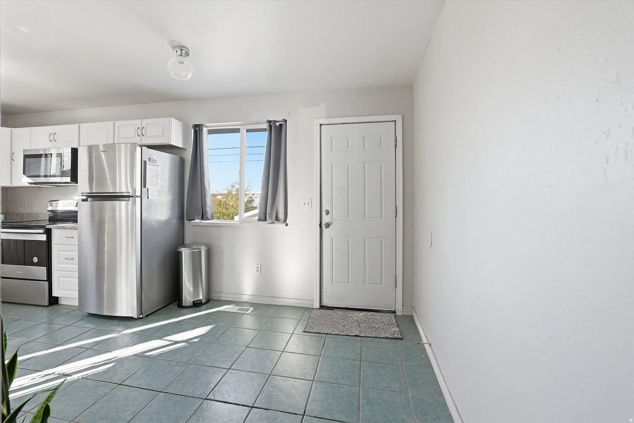 Kitchen with appliances with stainless steel finishes, white cabinetry, and dark tile patterned floors